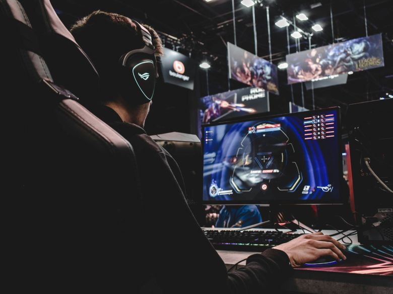 A photo of a man gaming competitively. He is wearing headphones and seated in a gaming chair, facing a PC screen and using a keyboard and mouse