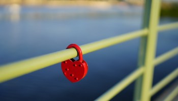 Red heart-shaped padlock on a railing over water