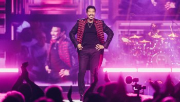 Photo showing Lionel Richie standing with hands on hips on a stage, from the viewpoint of the audience.