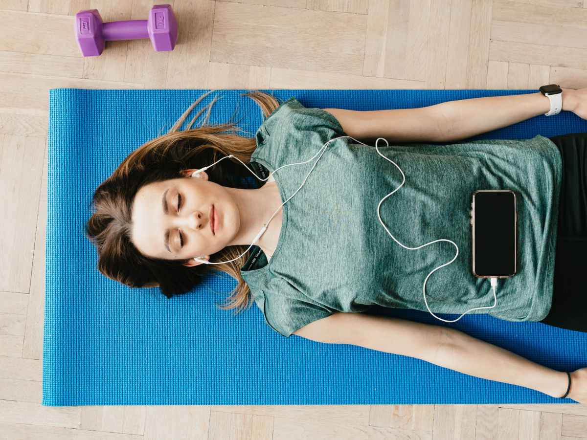peaceful woman in earphones resting in shavasana pose at home