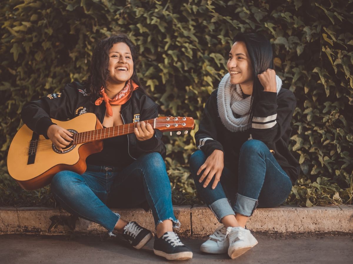 woman playing guitar sitting beside with woman wearing scarf