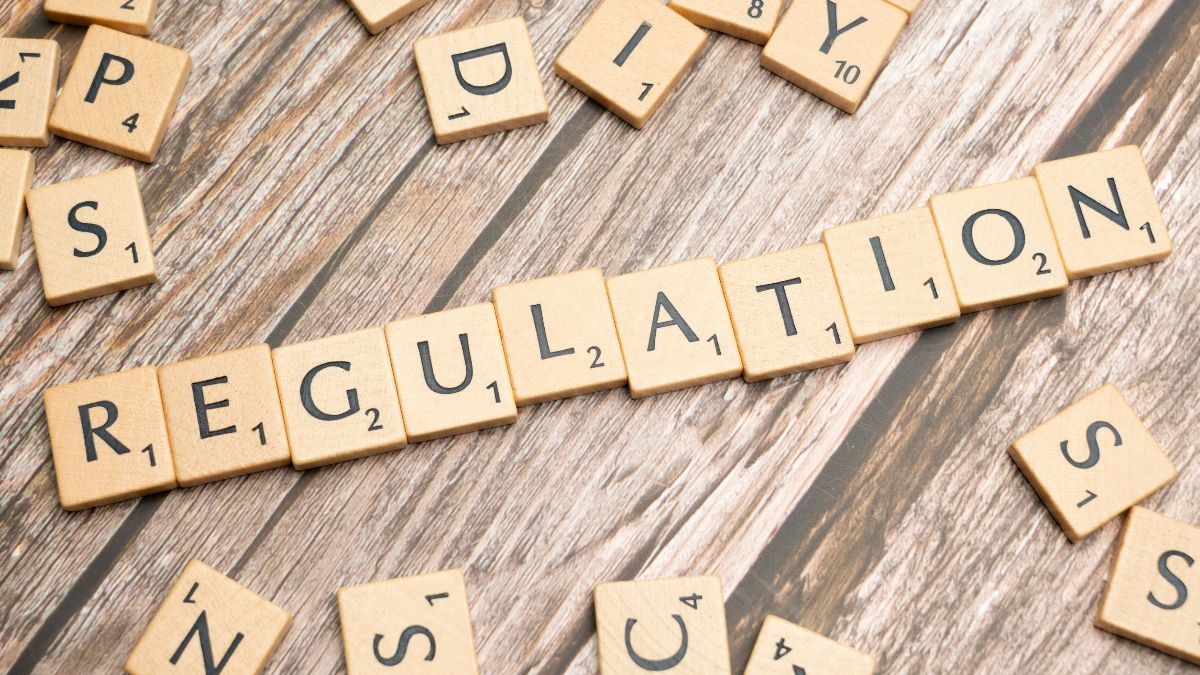 Scrabble tiles on a wooden table, with letters arranged to spell the word 'regulation'