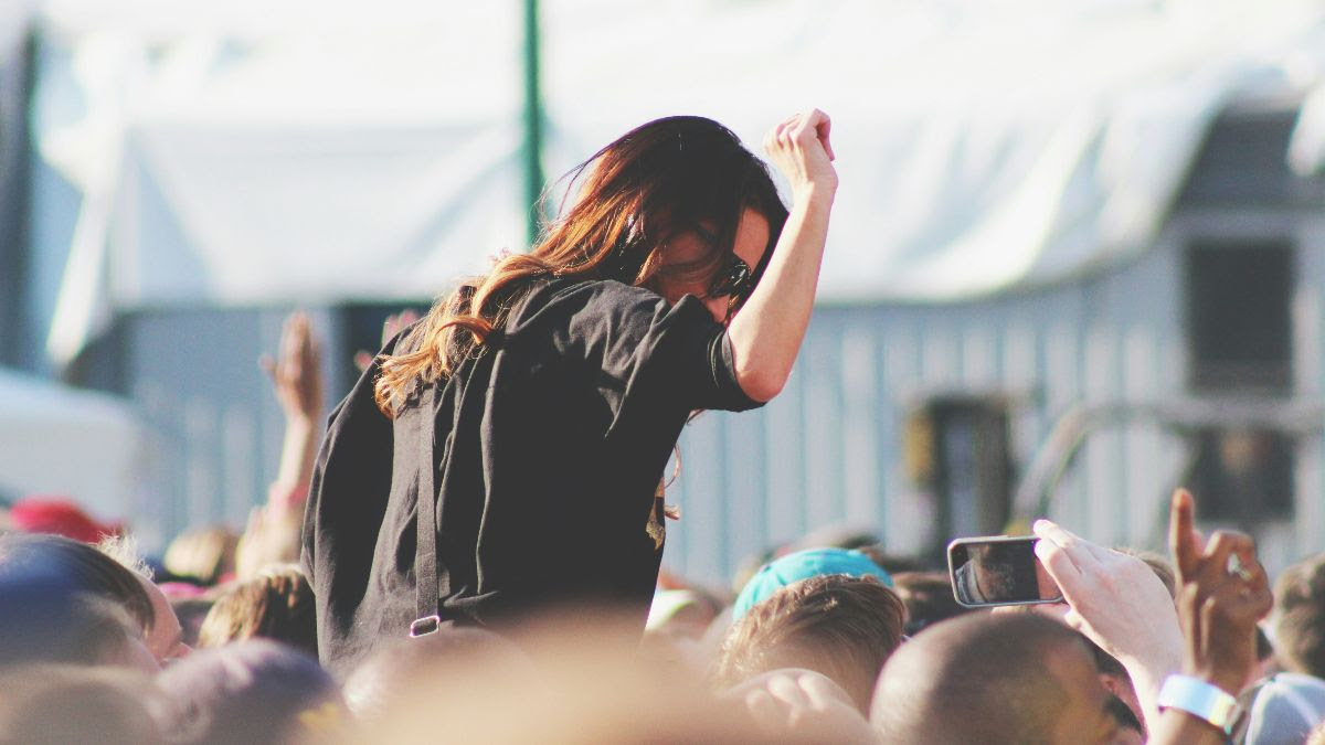 A young woman, shot from behind, on the shoulders of a person in a large crowd