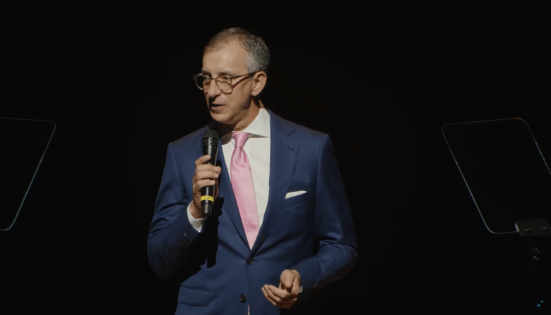 Photo of David Israelite. He is dressed in a dark blue suit and speaking into a handheld microphone.